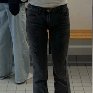 Svarta bootcut jeans - Snygga svarta bootcut jeans med låg midja och slitna detaljer. Perfekta för en avslappnad stil. De har en klassisk femficksdesign och en knappgylf.