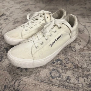 Vita sneakers från Juicy Couture - Snygga vita sneakers från Juicy Couture med klassisk snörning och märkets logga i svart glitter på sidan. Perfekta för en avslappnad stil. 