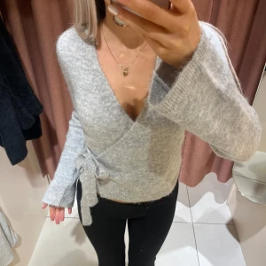 Grå omlottkofta från ginatricot storlek xs - Säljer en mysig grå omlottkofta med knytning i sidan. Koftan har långa ärmar och en v-ringad design som ger en stilren look. Perfekt för kyligare dagar. Storlek xs. Använd en enstaka gång men tycker ej jag passar i grå 