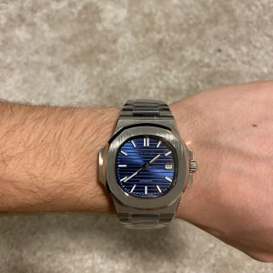 Seiko Nautilius Mod - Snygg Seiko herrklocka med en stilren blå urtavla och datumvisning. Boetten och armbandet är i silverfärgat stål. Klockan har lysande visare och index för enkel avläsning i mörker. Perfekt för den som vill ha en tidlös och elegant accessoar. Automatisk urverk och 40mm i storlek