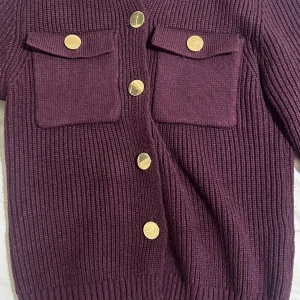 Vinröd ribbad kofta med guldknappar - Snygg vinröd kofta med ribbad struktur och dekorativa guldknappar. Två praktiska fickor framtill ger en stilren look. I storlek S och endast använd 2-3 gånger💕