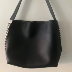 Svart axelväska med kedjedetalj Givenchy - Snygg svart axelväska i skinn med en stilren design. Väskan har en bred axelrem och en iögonfallande kedjedetalj på sidan. Perfekt för att ge en edgy touch till din outfit.