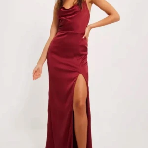 Vinröd långklänning med slits - Elegant vinröd långklänning i satin med smala axelband och en djup slits. Klänningen har en draperad halsringning och öppen rygg, perfekt för festliga tillfällen. Dem egna bilderna är från en inspelad video, så inga toppen foton :/ Kan skicka fler 