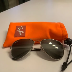 Solglasögon från Ray-Ban - Snygga solglasögon från Ray-Ban med klassisk pilotform och silverfärgad metallram. De har silvrigt glas som ger ett coolt och stilrent intryck. Perfekta för soliga dagar och kommer med en orange förvaringspåse med Ray-Ban-logga.