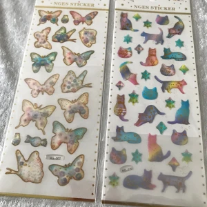 Färgglada klistermärken - Säljer ett set med färgglada klistermärken från NGES. Setet innehåller olika motiv som fjärilar, katter, havsdjur, hjärtan och sötsaker. Perfekt för att dekorera anteckningsböcker, kort eller andra kreativa projekt. Klistermärkena har en glittrig och lekfull design.  48kr/2st/bild 