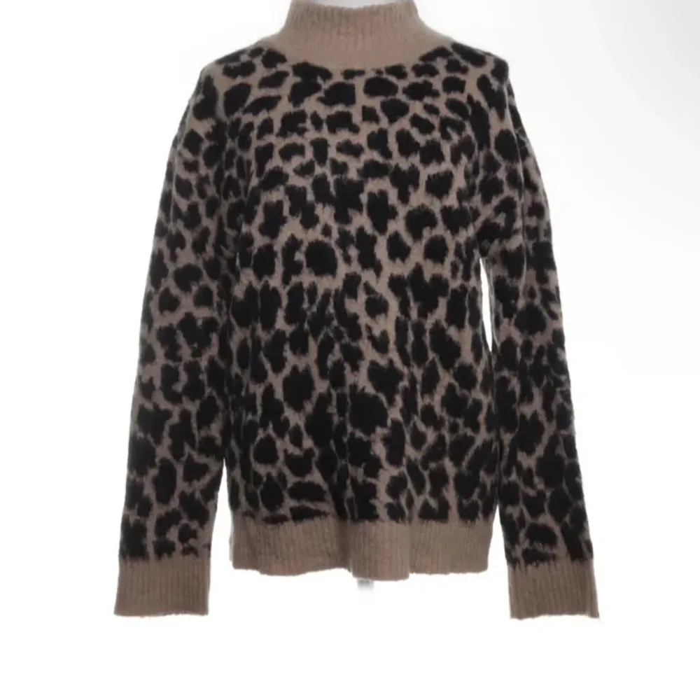 Säljer en snygg leopardmönstrad stickad tröja med hög krage. Tröjan har långa ärmar och ribbade muddar vid ärmslut och nederkant. Perfekt för att hålla sig varm och trendig.. Neuletakit & Villapaidat.