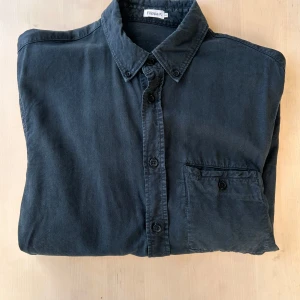 Mörkblå skjorta från Filippa K - Snygg mörkblå button-down skjorta från Filippa K. Skjortan har en bröstficka och långa ärmar med knappar vid ärmsluten. Färgen är, från fabrik, lite sotig. Den är mörkblå, men övergår ibland till lite ljusare och mer ”slitna” partier.