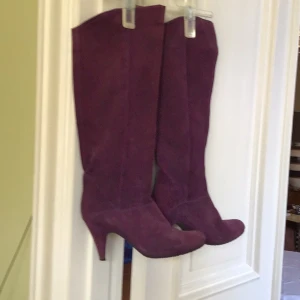 Lila mockastövlar med klack - Snygga lila stövlar i mocka med klack. Perfekta för att ge en färgklick till din outfit. De har en elegant design med spetsig tå och är tillverkade i ett mjukt material.
