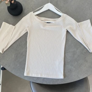 Beige/cremefärgad  topp från Gina Tricot - Säljer en stilren topp från Gina Tricot. Toppen har långa ärmar och en bekväm passform. Perfekt för en avslappnad look. Passar både som en vanlig tröja och off shoulder