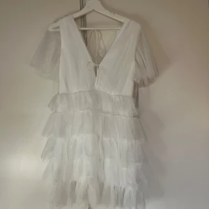 Vit klänning med volanger från Bubbleroom - Säljer en söt vit klänning från Bubbleroom med flera lager av volanger och knytning i ryggen. Klänningen har korta ärmar och en v-ringad design. Perfekt för sommarens alla tillfällen! 🌸Köpt för 1 månad sedan för att ha på studenten men hitta en ny så säljer denna nu, aldrig använd endast testad! 