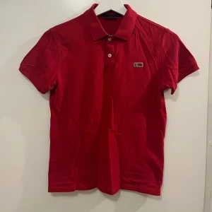 Röd pikétröja från Napapijri - Snygg röd pikétröja från Napapijri med klassisk krage och knappslå. Den har en liten logotyp på bröstet