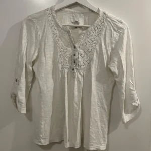 Vit blus från H&M - Säljer en söt vit blus från H&M med vackra spetsdetaljer och knappar framtill. Blusen har trekvartsärmar och en avslappnad/ tight passform