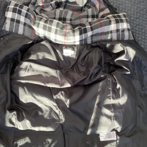 Svart pufferjacka från Burberry - Säljer en snygg svart pufferjacka från Burberry med ett klassiskt rutigt mönster på insidan. Jackan har en quiltad design och en dragkedja framtill. Perfekt för kyliga dagar!