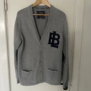 Grå kofta från Bondelid - Säljer en stilren grå kofta från Bondelid med mörkblå detaljer. Koftan har långa ärmar och knappar framtill samt två fickor. Perfekt för en avslappnad look. Skriv om ni har några övriga frågor🙌