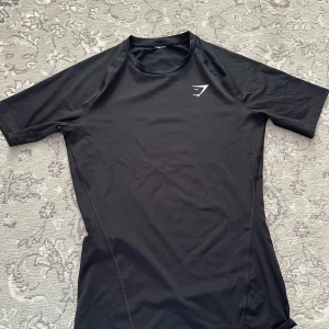 Svart compression shirt från Gymshark - Snygg och funktionell svart t-shirt från Gymshark. Perfekt för träning med sin bekväma passform och korta ärmar. Diskret logga på bröstet ger en stilren look.