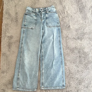 Blå jeansbyxor från Zara - Säljer ett par snygga blå jeansbyxor från Zara. De har en elastisk midja och stora framfickor. Perfekta för en avslappnad stil med en loose passform.