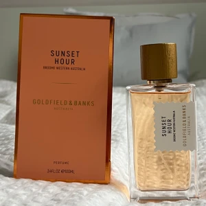 Sunset Hour Parfym från Goldfield & Banks - Upptäck Sunset Hour, en lyxig parfym från Goldfield & Banks inspirerad av Broome, Western Australia. Flaskan har en elegant design med en gyllene kork och en etikett i vitt. Doften kombinerar toner av italiensk mandarin, ökenpersika och hallon med inslag av sandelträ och vanilj. Ungefär 98ml kvar.