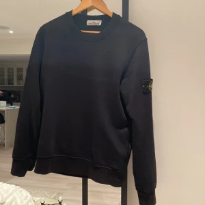 Svart sweatshirt från Stone Island - Säljer en stilren svart sweatshirt från Stone Island. Tröjan har en rund halsringning och långa ärmar med den ikoniska logotypen på ärmen. Perfekt för en casual look. 🖤