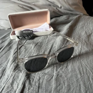 Transparenta solglasögon från Montén - Snygga transparenta solglasögon från Montén med mörka linser. Perfekta för en stilren look. Kommer med ett elegant fodral och putsduk.