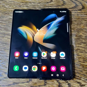 Samsung Galaxy Z Fold4 - Säljer en Samsung Galaxy Z Fold4 med en innovativ vikbar design. Telefonen har en stor, vikbar skärm och en elegant vit baksida med trippelkamera. Perfekt för multitasking och en unik mobilupplevelse.