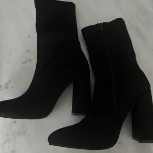 Svarta sock boots med klack - Snygga svarta stövletter med hög klack och spetsig tå. De har en dragkedja på sidan för enkel på- och avtagning. Perfekta för att ge en elegant touch till din outfit. Använda 1 gång, ser helt nya ut