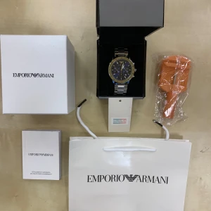  Armani klocka  - Säljer en stilren Emporio Armani klocka med blå urtavla och silverfärgad länkarmband. Klockan har en tachymeter och flera sub-dials för extra funktionalitet. Perfekt för den som vill ha en elegant accessoar.