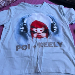 Ljusblå t-shirt från Bershka - Cool ljusblå t-shirt från Bershka med ett unikt tryck av en figur med hörlurar och texten 'Poi + Keely'. Perfekt för en avslappnad stil. Tillverkad i Turkiet.
