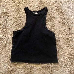 Svart ribbad linnetopp från Weekday - Säljer en stilren svart ribbad linnetopp från hm Perfekt för varma dagar eller som lager under en jacka. Toppen har en enkel och tidlös design med rund halsringning.