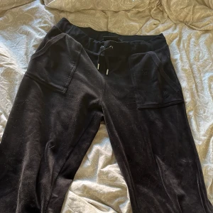 Svarta mjukisbyxor från Juicy Couture - Snygga svarta mjukisbyxor från Juicy Couture med snörning i midjan och praktiska fickor. Perfekta för en avslappnad stil. Byxorna har en broderad logga på fickan och är gjorda i ett mjukt material. Säljer för de är för stora för mig