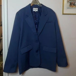 Blå kavaj från NA-KD - Snygg blå kavaj från NA-KD med klassisk design och två knappar framtill. Kavajen har en normal passform och är perfekt för en stilren look. Den har långa ärmar och fickor. Använd fåtal gånger. Otroligt snygg nu till våren, perfekt till tidiga vårkvällar. 