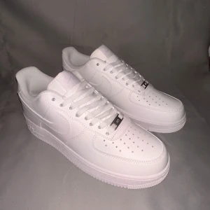 Vita Nike Air Force sneakers - Säljer ett par klassiska vita Nike Air Force sneakers. De har en stilren design med snörning och perforerade detaljer på tån för extra ventilation. Perfekta för en clean och tidlös look.