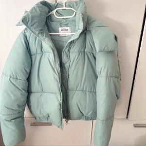 Ljusgrön pufferjacka från Weekday - Säljer en ljusgrön pufferjacka från Weekday. Jackan har en dragkedja framtill och en hög krage för extra värme. Perfekt för kyliga dagar med sin vadderade design. Har 2 fläckar ( på sidan och en på armen) 