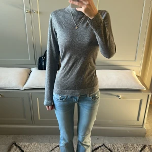 Grå glittrig tröja - Snygg grå tröja med glittrig finish. Perfekt för att ge lite extra bling till din outfit. Tröjan har en hög krage och långa ärmar, vilket gör den både stilren och bekväm.