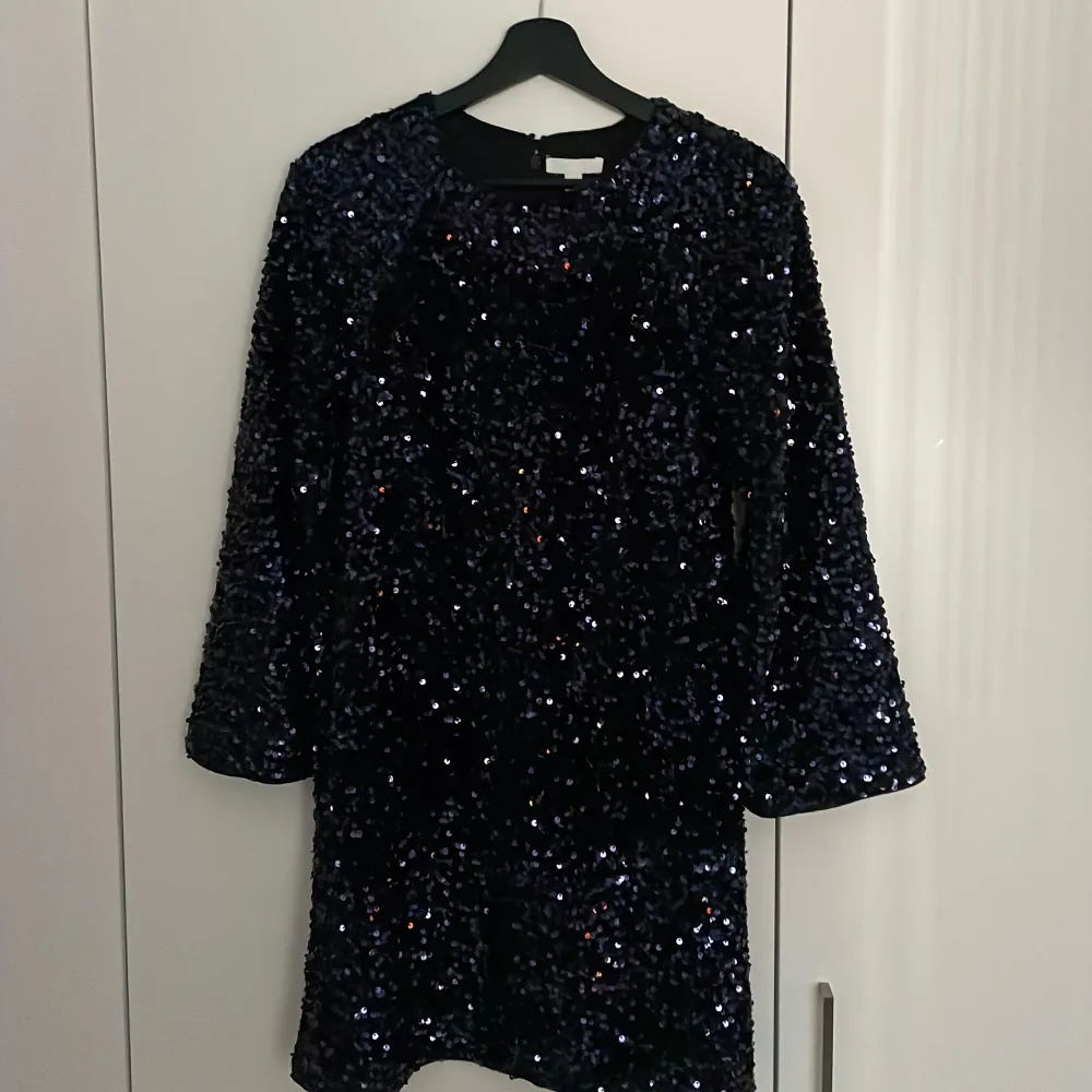 Snygg lila klänning täckt med glittriga paljetter. Den har trekvartsärmar och en bekväm passform som gör den perfekt för festliga tillfällen. Klänningen är både elegant och iögonfallande.. Mekot.