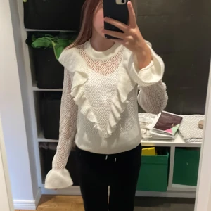 Vit spetsblus med volangdetaljer - Säljer en elegant vit blus med spets och volangdetaljer. Blusen har långa ärmar och en rund halsringning. Perfekt för en stilren look.