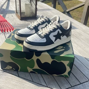 Svartvita sneakers från Bape - Snygga svartvita sneakers från Bape med en ikonisk stjärndetalj på sidan. Skorna har snörning och en klassisk siluett. De kommer i en cool kamouflagemönstrad låda. Creaseslydd ingår