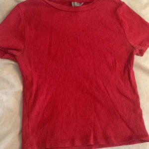 Röd ribbad topp - Säljer en snygg röd ribbad topp med korta ärmar. Perfekt för en casual look. Toppen har en rund halsringning och är gjord i ett stretchigt material som ger en bekväm passform.