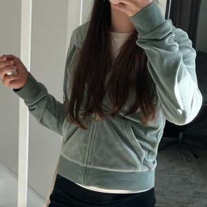 Grön hoodie från Juicy Couture - Snygg och bekväm grön hoodie från Juicy Couture i mjuk sammet. Den har dragkedja framtill och en klassisk huva. Perfekt för en avslappnad stil. Fickan på ena sidan så har sonen gott upp men går att fixa hur lätt som helst🥰