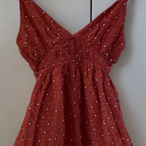 super fin mörkröd blus  -  Säljer en söt röd blus från mango med mönster. Klänningen har en smickrande v-ringning och är ärmlös, perfekt för varma dagar. Den har en elastisk midja som ger en utsvängd fin passform 