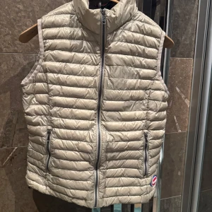 Beige dunväst från Colmar - Snygg beige dunväst från Colmar med dragkedja framtill och två praktiska fickor med dragkedjor. Perfekt för lager-på-lager under kyligare dagar. Västen har en stilren design och är lätt att matcha med olika outfits.  EU 38