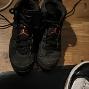 Svarta Nike Air Jordans med röda detaljer - Säljer ett par svarta Nike Air Jordans med röda detaljer. Skorna har en klassisk design med snörning och den ikoniska Jumpman-loggan i rött. Perfekta för dig som vill ha en stilren och sportig look.