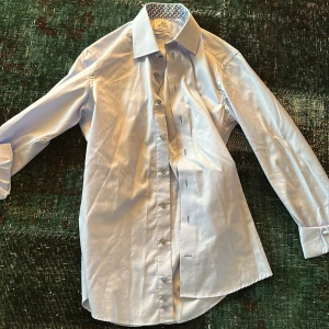 Ljusblå skjorta från XO Sand - Snygg ljusblå skjorta från XO Sand i slim fit med ett stilrent mönster på insidan av kragen. Skjortan har långa ärmar och knappar framtill. Perfekt för en elegant look. Storlek sitter som S