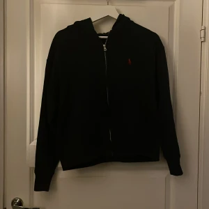 Mörkblå hoodie från Polo Ralph Lauren - Säljer en stilren mörkblå hoodie från Polo Ralph Lauren med dragkedja och röd logga på bröstet. Perfekt för en avslappnad look. Den har långa ärmar och en praktisk huva.Använd 2 gånger 💞