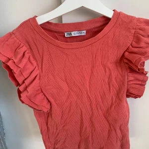 Rosa ribbad topp från Zara - Säljer en söt rosa ribbad topp från Zara med volangdetaljer på ärmarna. 