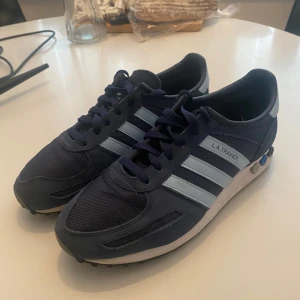 Adidas LA Trainer  - Snygga Adidas LA Trainer sneakers i marinblått med de klassiska tre ränderna i ljusblått på sidan. Skorna är köpta från DIF butiken för 1200 ish och priset kan diskuteras. 