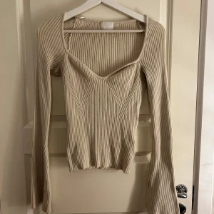 Beige ribbad tröja från H&M - Säljer en stilren beige ribbad tröja från H&M med v-ringning och långa ärmar. Perfekt för en chic och bekväm look. Tröjan har en figurnära passform som framhäver silhuetten. Passar utmärkt till både jeans och kjol.