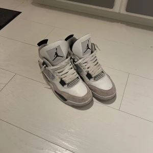 Nike Air Jordans i vit och grå - Säljer ett par stilrena Nike Air Jordans i vit och grå med svarta detaljer. Skorna har en klassisk design med snörning och den ikoniska loggan på plösen och sulan. Perfekta för dig som vill ha en sportig look. Priset kan diskuteras. Du får med crees skydd Och du får med lådan.