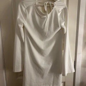 Vit långärmad klänning med knyt - Elegant vit klänning med långa ärmar och knytning fram. Perfekt för en stilren look. Materialet ger en fin struktur och klänningen har en klassisk passform. Den är helt ny med prislapp💕