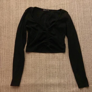 Svart croppad topp från Zara - Säljer en svart croppad topp från Zara med långa ärmar och en snygg rynkad detalj framtill. Perfekt för en stilren look. 🖤