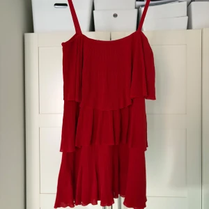 Röd klänning från Zara - Säljer en röd klänning från Zara med volanger och smala axelband. Klänningen har en luftig design med flera lager och är perfekt för varma dagar. Den är öite skimrig i materialet